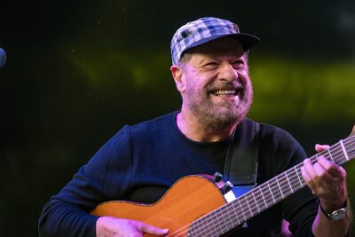João Bosco smiling as he plays a nylon-string guitar on stage in Belo Horizonte in 2024