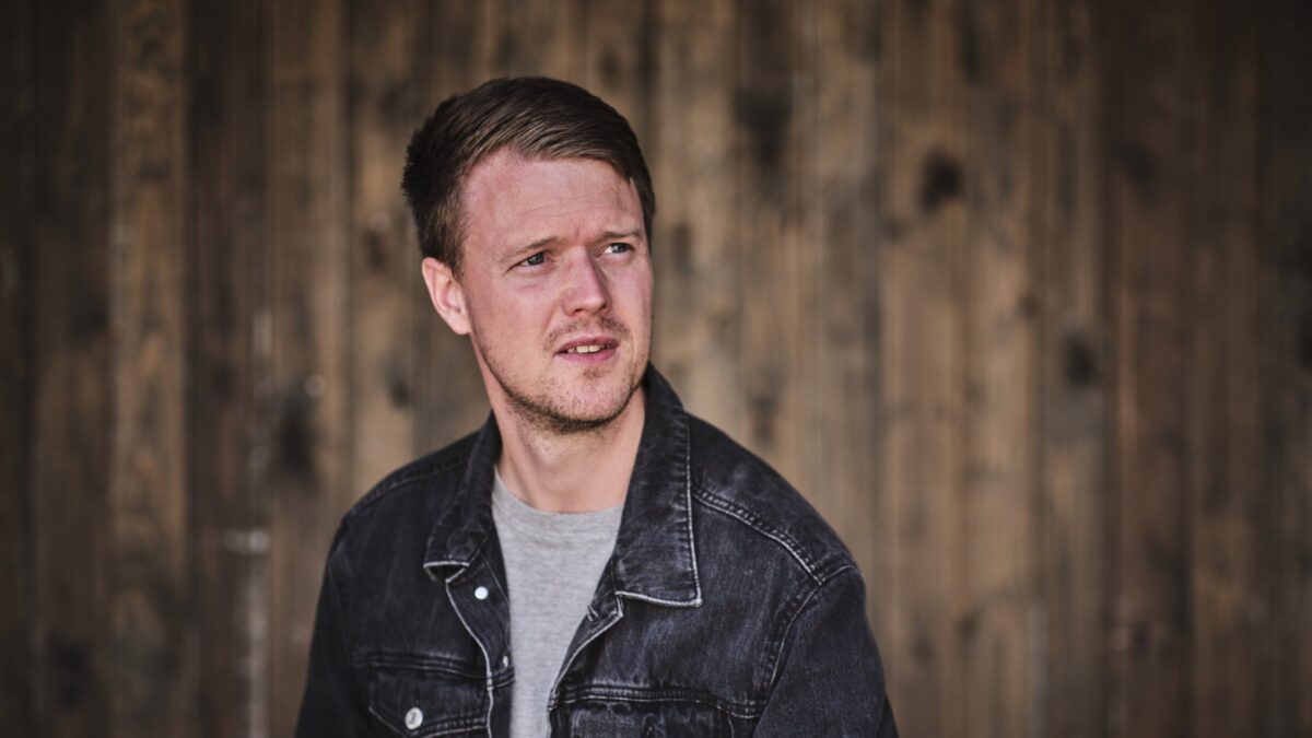 Kasper Buch in a denim jacket against a weathered wooden wall