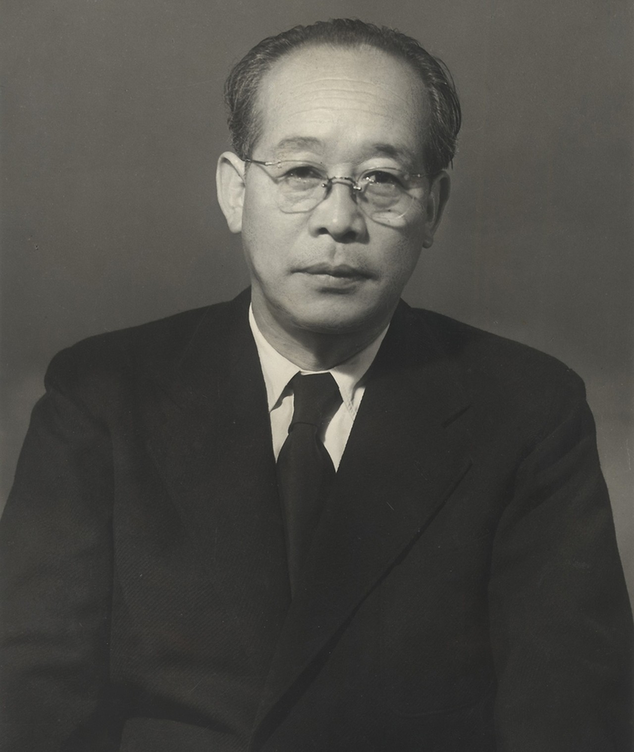 Kenji Mizoguchi in a studio portrait from the 1950s, wearing round glasses and a dark suit
