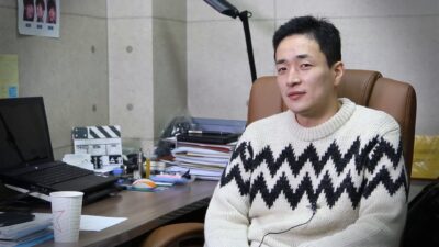 Director Lee Byeong-heon in a white zigzag sweater at his office desk during a 2015 interview for Twenty