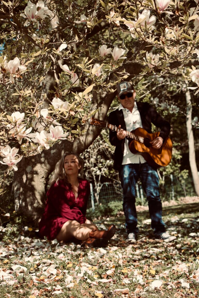 Susanne Kristensen seated beneath a magnolia tree as Jan Kolle plays acoustic guitar