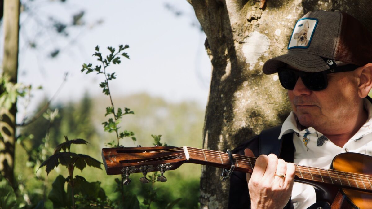 Magnolia Shade songwriter Jan Kolle playing acoustic guitar against a tree