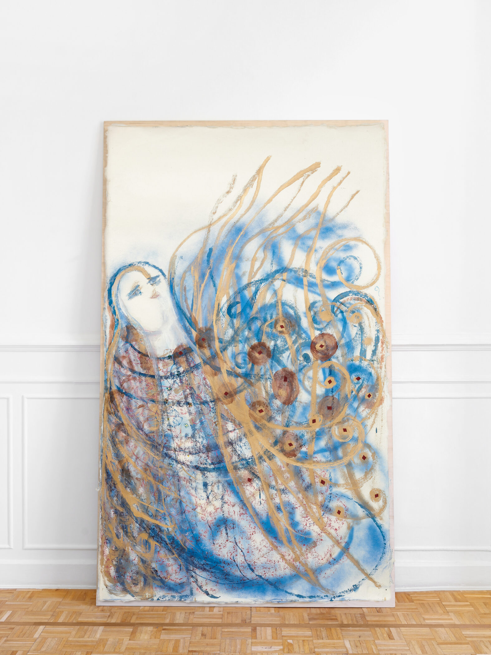 Marisa Merz painting Senza Titolo, a pale face amid swirling blue and gold lines on a large unframed sheet leaning against a white wall