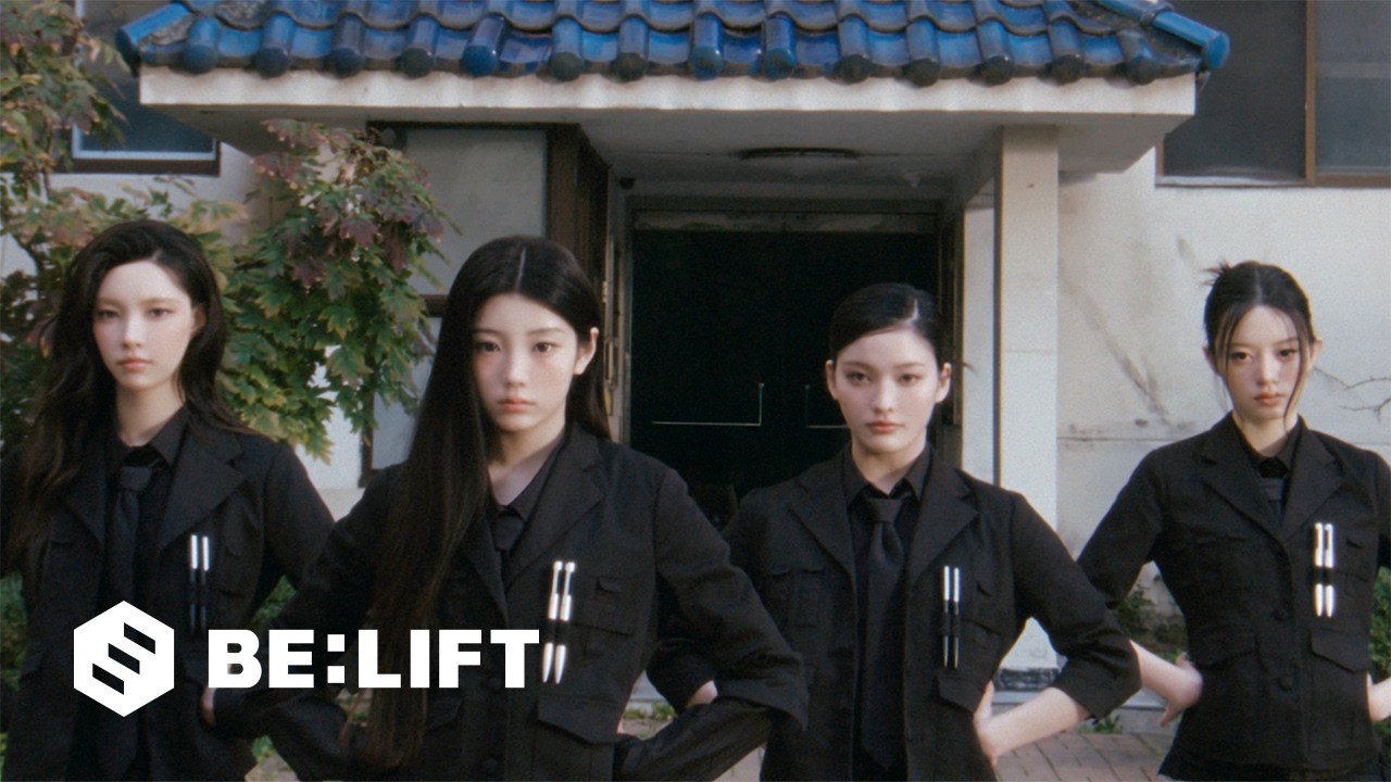 The four promoting members of ILLIT in black agent suits outside a tiled-roof building in the You're Under Arrest music video