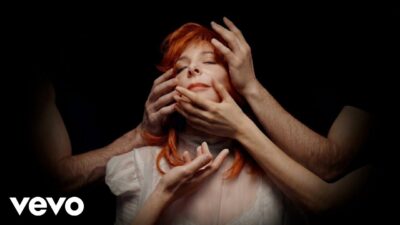Mylène Farmer with eyes closed as several hands hold her face, from the Égrégore visualizer