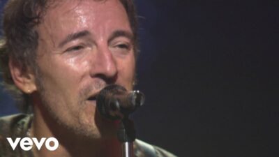 Bruce Springsteen singing into a microphone on stage at the Palau Sant Jordi in Barcelona