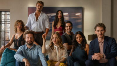 The eight-member ensemble of Friends Sex and Games posed in a living room, with the woman seated at the centre holding up a set of keys