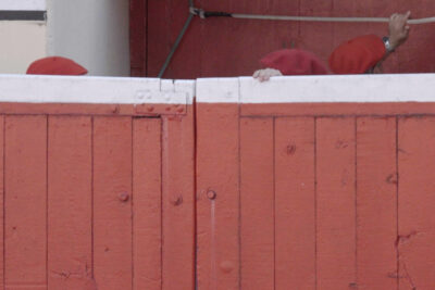 Video still from Paul Pfeiffer Pasodoble: red berets and a hand gripping the top of a red and white bullring barrier