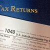 A US Form 1040 individual income tax return resting on a blue Tax Returns folder