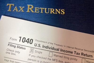 A US Form 1040 individual income tax return resting on a blue Tax Returns folder