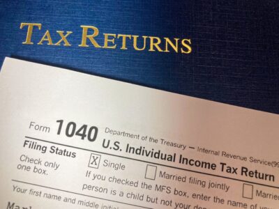 A US Form 1040 individual income tax return resting on a blue Tax Returns folder