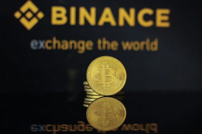 Binance logo behind a gold Bitcoin coin on a dark reflective surface — Bastian Riccardi / Pexels