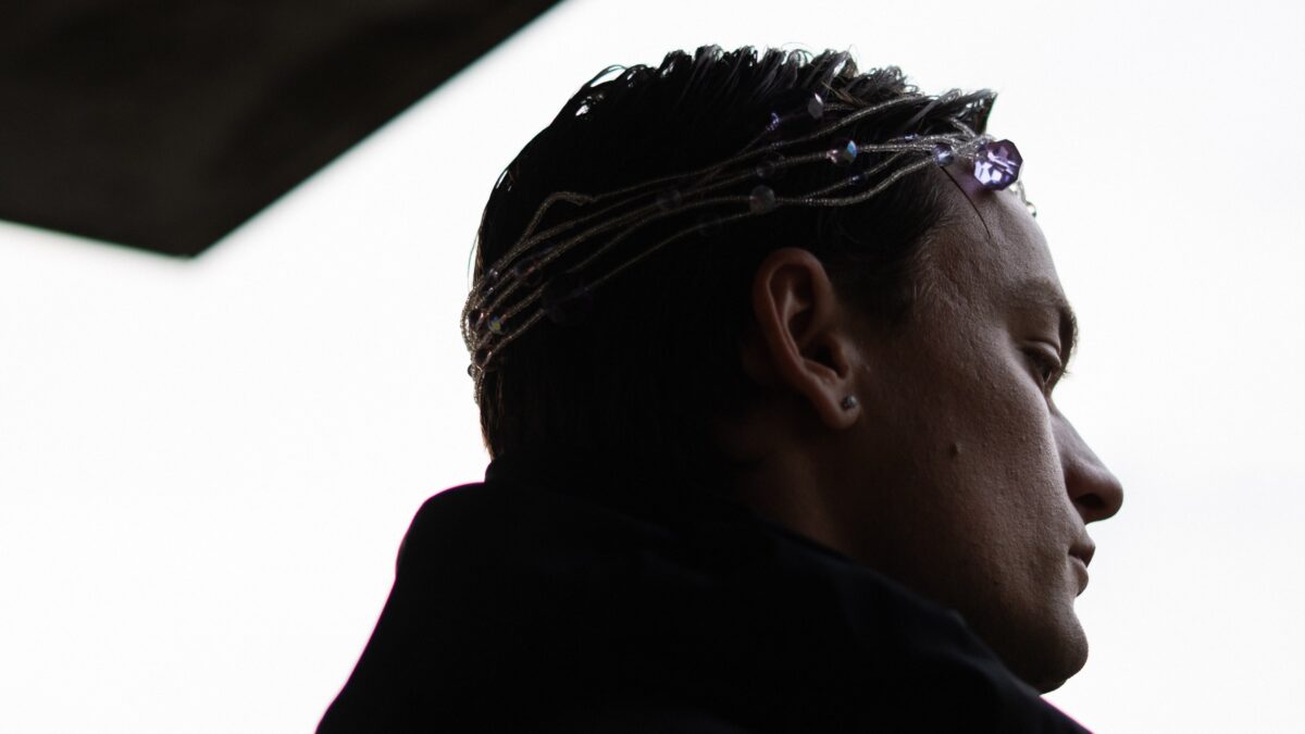 Romyo in profile wearing a beaded crystal headpiece against a pale sky