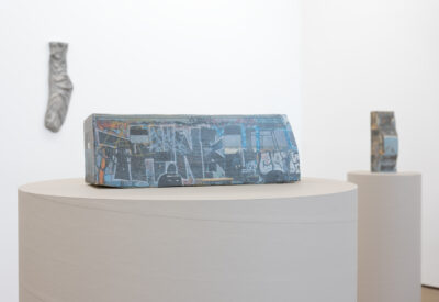 Ry Rocklen ceramic bus sculpture Slice of Life on a white plinth with a cast sock on the wall