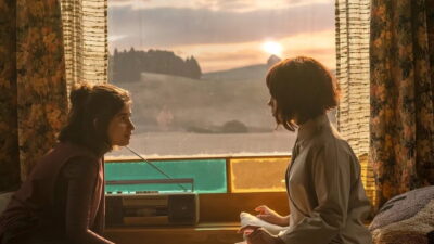 Jenna Ortega as Klara at a farmhouse window facing a low sun in a still from Taika Waititi’s Klara and the Sun