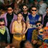 The members of Ecuadorian band Swing Original Monks in sunglasses and colourful outfits amid a confetti-strewn party crowd