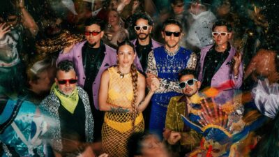 The members of Ecuadorian band Swing Original Monks in sunglasses and colourful outfits amid a confetti-strewn party crowd