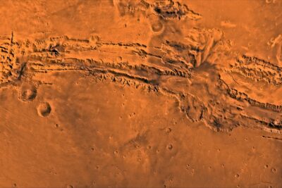 Western Valles Marineris on Mars seen from orbit: long parallel canyon walls cutting east across orange plains, with the maze of Noctis Labyrinthus at left