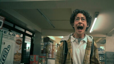 Diego Bernal as Archie screaming inside a fluorescent-lit corner shop in a still from the Prime Video series I Would Rather Die