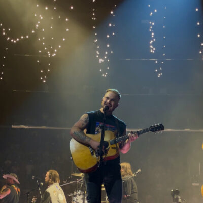 Zach Bryan singing with an acoustic guitar on stage at Crypto.com Arena in Los Angeles in August 2023