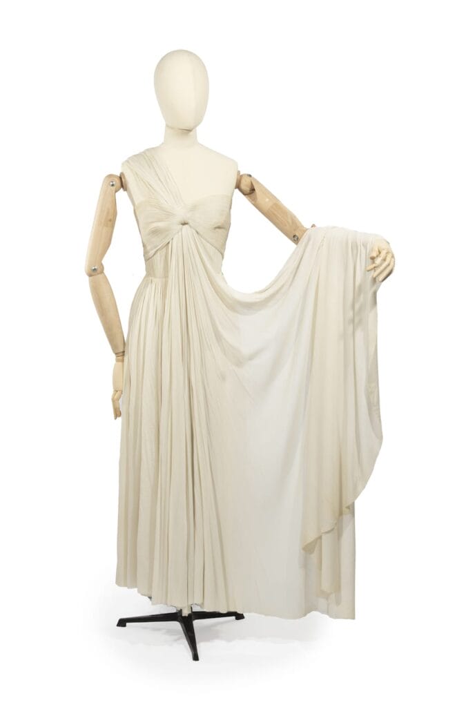 Grès, collection Haute Couture, circa 1955 Prototype du défilé  Robe de cocktail sans manches, petit col, effet de taille plissée, jupe fluide, mousseline de soie beige. Griffe blanche, graphisme noir « Grès 1 rue de la Paix Paris - Made In France « - Plomb de douane   Provenance: Archives personnelles d’Alix Grès  - Collection maison Jacques Esterel. - Collection Quidam de Revel.   Exposition: Madame Grès, entre Ombre et Lumière, Bourgoin-Jallieu du 19 juin 2004 au 31 janvier 2005 1 000 - 1 500 euros